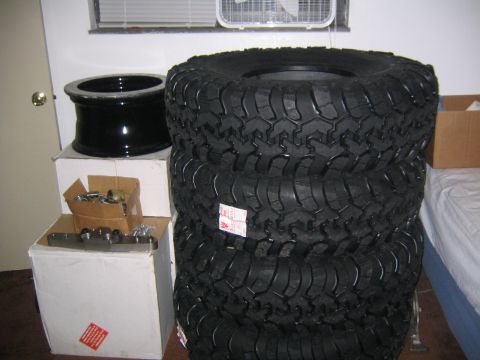 1978 Ford Bronco - Four large off-road tires are stacked next to a single black wheel, with boxes and hardware visible.