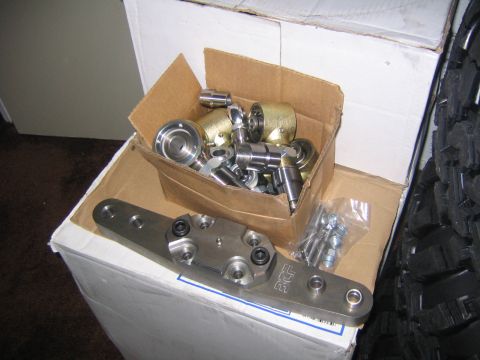 1978 Ford Bronco - Various metal automotive parts, including rod ends and a steering bracket, are laid out on boxes.