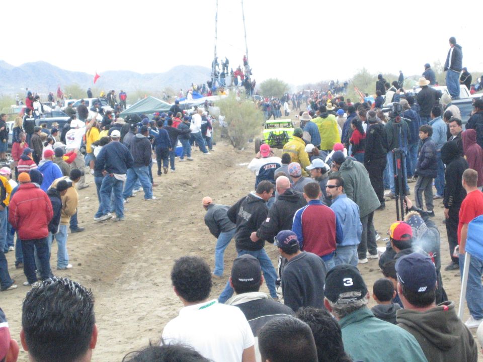 Spectators on a dirt desert course watching a distant off-road buggy