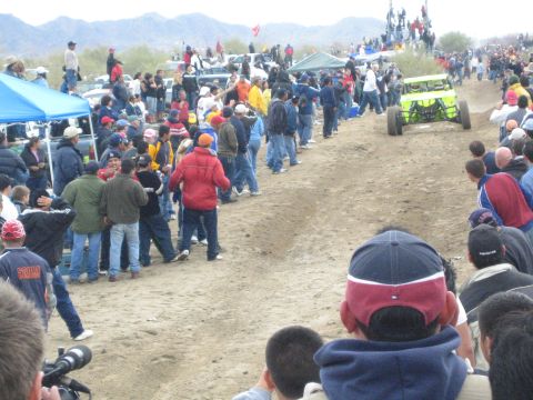 1990 Ford Bronco - bright green off-road buggy runs the dirt course as crowds and a blue tent line the desert track.