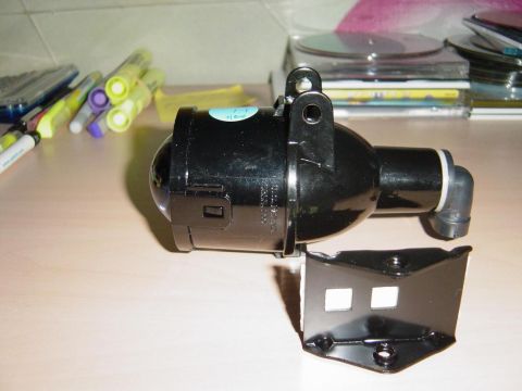 1993 Ford Probe - A black headlight assembly with its mounting bracket is shown on a table, with office supplies in the background.