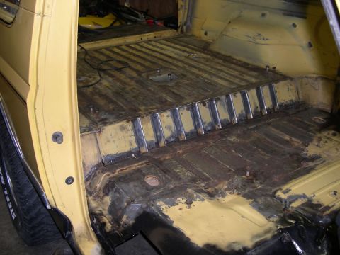 1982 Ford Bronco - The interior floor of a yellow vehicle shows significant rust and recent metal work.