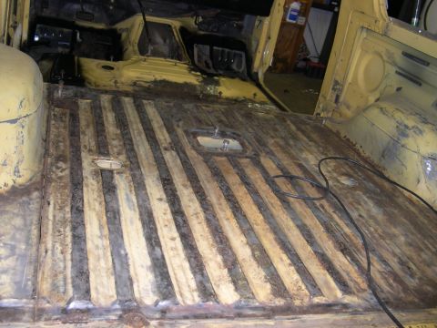 1982 Ford Bronco - The interior cargo area of a yellow vehicle shows a ribbed floor with significant rust and wear.