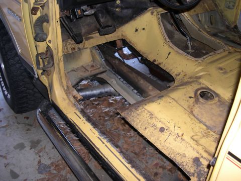 1982 Ford Bronco - The interior of a yellow vehicle displays significant rust damage on the floor pan and rocker panel.