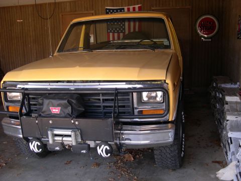 1982 Ford Bronco - Front view of a yellow pickup truck with a winch and KC lights, parked indoors.