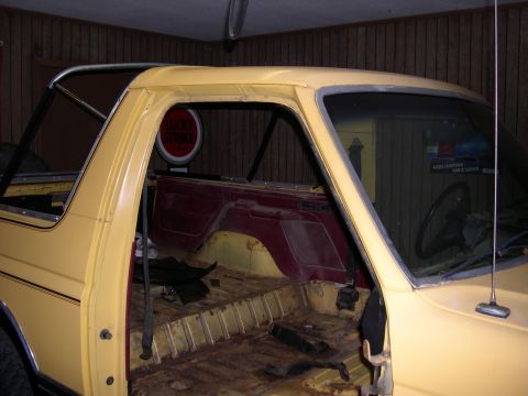 1982 Ford Bronco - This Bronco's interior is stripped down, revealing the floor and red side panels. A vintage sign hangs in the background.