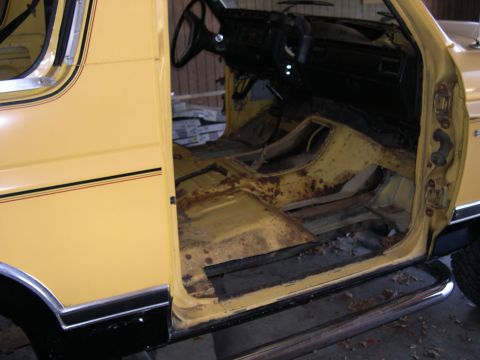 1982 Ford Bronco - The interior of a yellow SUV shows significant rust and damage, indicating a need for restoration.