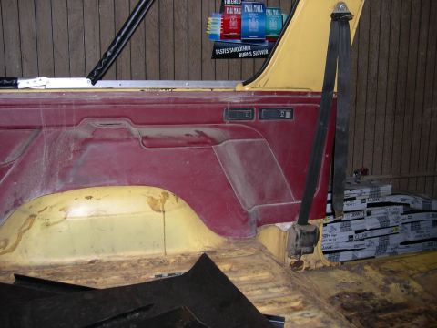 1982 Ford Bronco - The interior of the vehicle shows worn red and yellow panels, with a seatbelt and stacks of boxes in the background.