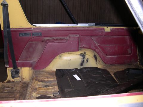 1982 Ford Bronco - The interior of a vehicle shows worn floorboards and maroon door panels.