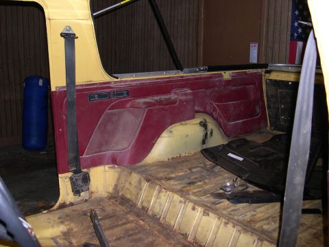 1982 Ford Bronco - The interior of a vehicle shows yellow flooring and red door panels, with a seatbelt visible.