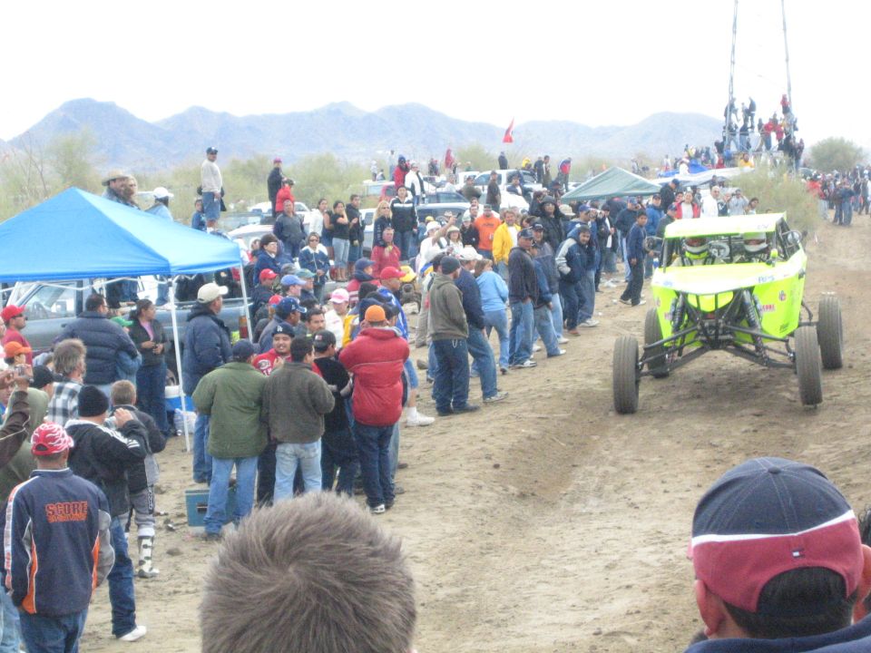 Green and white off-road buggy on a dirt course lined with crowds