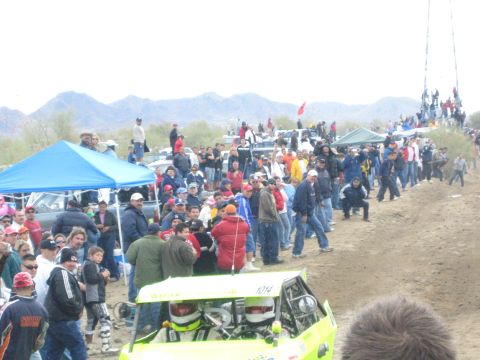 1990 Ford Bronco - green-yellow off-road buggy marked 1014 sits near the dirt course as spectators and a blue tent fill the desert background.