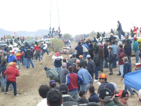 1990 Ford Bronco - Spectators crowd a dirt desert course where a small buggy is visible and people watch from a distant tower.