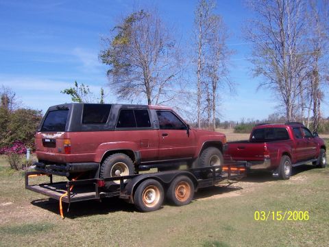 1984 Toyota 4Runner - A red 1984 Toyota 4Runner is transported on a trailer, towed by a red pickup truck under a clear sky.