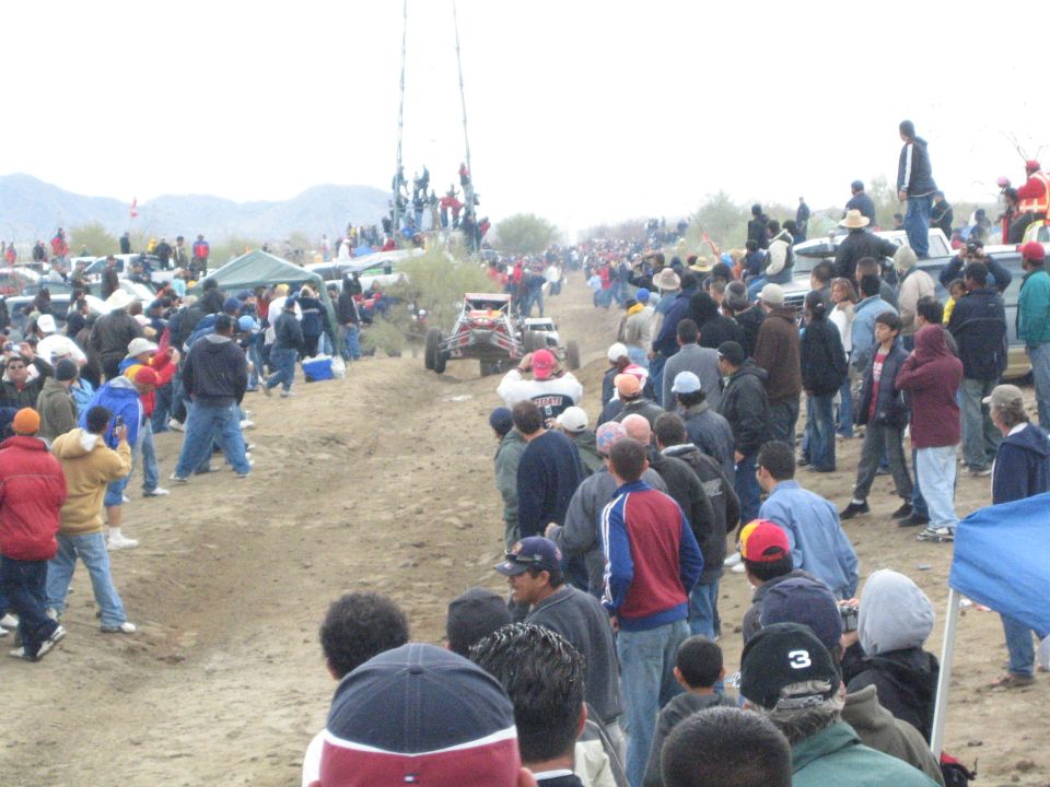 Single-seat off-road buggy on a dirt desert course lined by a large spectator crowd