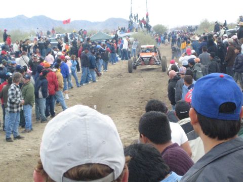 1990 Ford Bronco - off-road buggy runs a dirt desert course as spectators line both sides and red flags mark a distant rise.