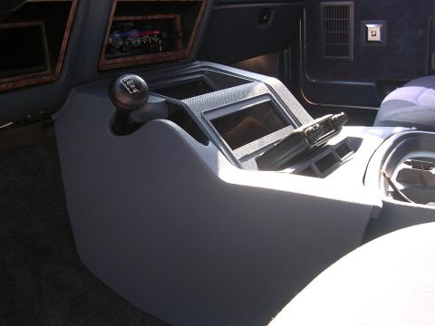 1986 Ford Bronco - The interior center console of a vehicle, a manual gear shifter and a radio mount.