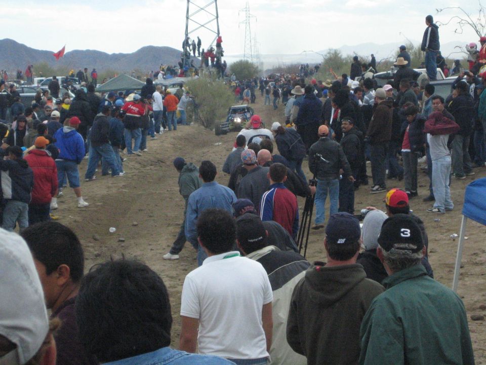Distant vehicle on a desert dirt course lined by very large crowds