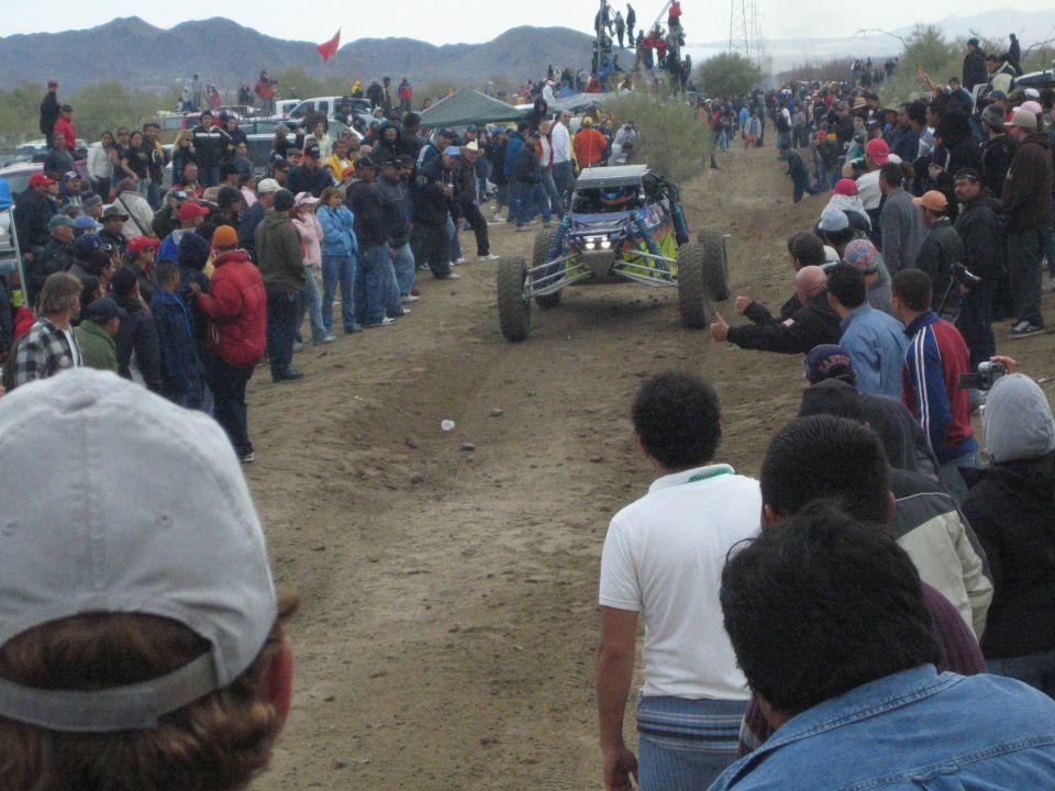 Blue off-road race buggy driving toward crowd on a desert dirt course