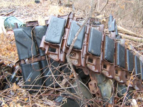 1942 Jeep CJ5 - Rusty tank tracks and several green jerry cans are piled up in an outdoor setting.