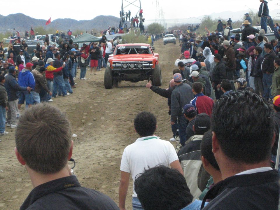 Red off-road truck number 800 driving down a dirt course past spectators