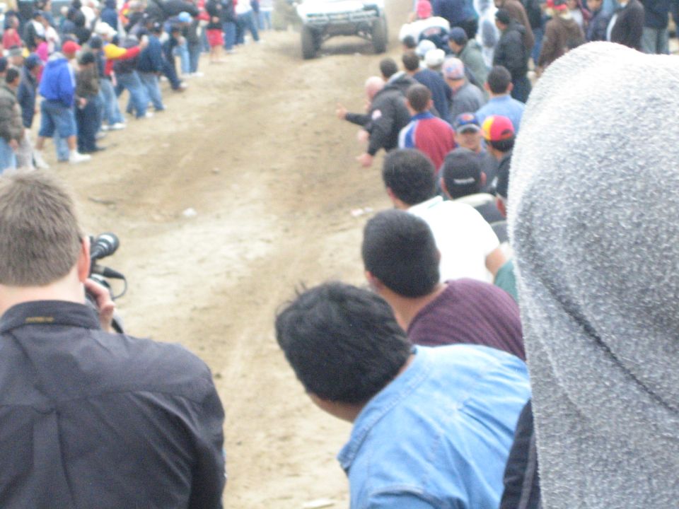 Distant off-road truck on a dirt course with spectators in foreground