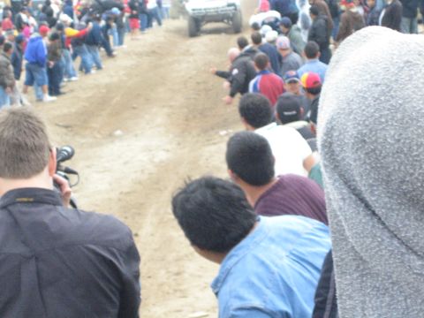 1990 Ford Bronco - distant off-road truck climbs a dirt course as spectators with a camera watch from the foreground in the desert.