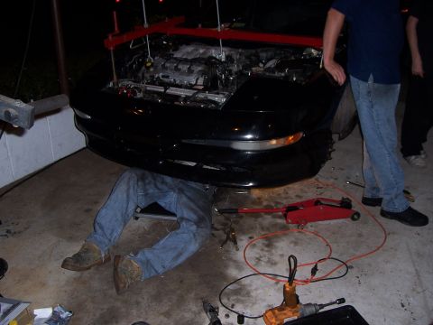 1994 Ford Probe - A mechanic works on a car's engine, which is supported by a red engine hoist.