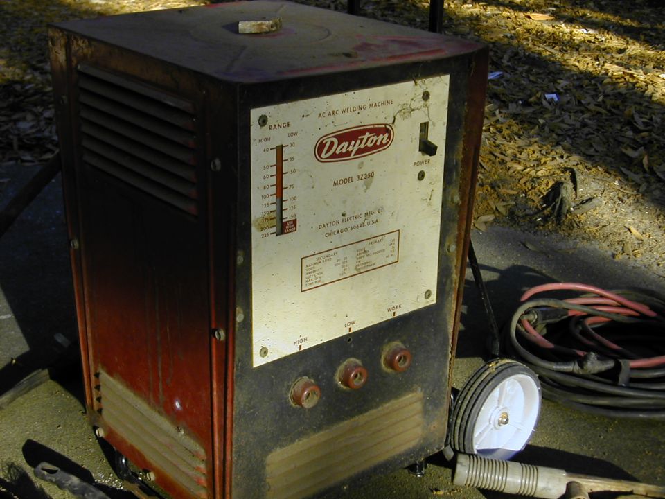 Old red Dayton 3Z350 AC arc welder outdoors with coiled welding leads on concrete