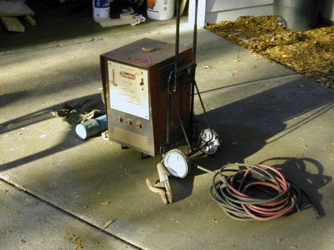 1993 Ford Bronco - An old red Dayton AC arc welder strapped to a two-wheel hand truck on a concrete driveway outside a garage, with coiled red and black weldi…