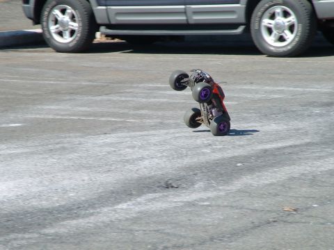 1994 Ford Bronco - A remote-controlled car performs a stunt on asphalt, with a larger vehicle partially visible.