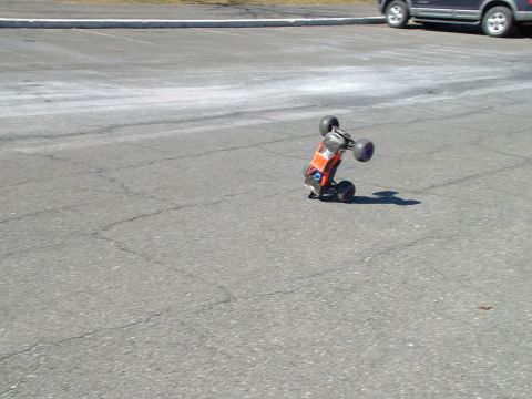 1994 Ford Bronco - An orange remote control car is captured mid-air, balancing on its rear wheels on an asphalt surface.
