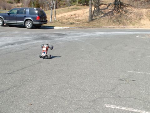 1994 Ford Bronco - A remote control monster truck is driving on asphalt with a blue SUV in the background.