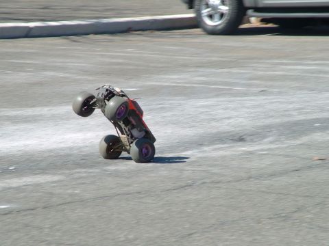 1994 Ford Bronco - A remote control monster truck is captured mid-air, balancing on its rear wheels on a paved surface.