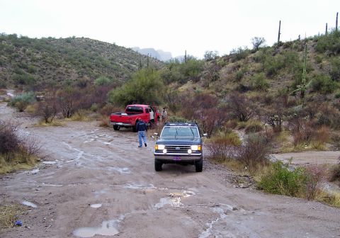1991 Ford Bronco - Two Ford trucks navigate a muddy desert track after rain.