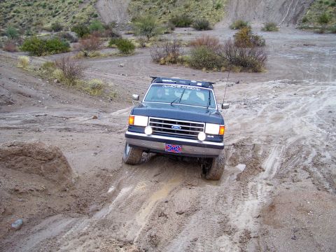 1991 Ford Bronco - This dark blue Ford Bronco navigates a challenging muddy terrain, its off-road capabilities.