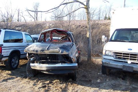 1977 Ford F-150 - This severely damaged truck, possibly a Ford F-150, is seen in a junkyard setting with other vehicles.