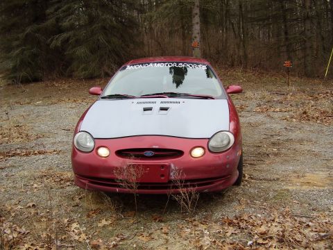 1997 Ford Taurus - Front view of a 1997 Ford Taurus with a silver hood, parked in a wooded area.