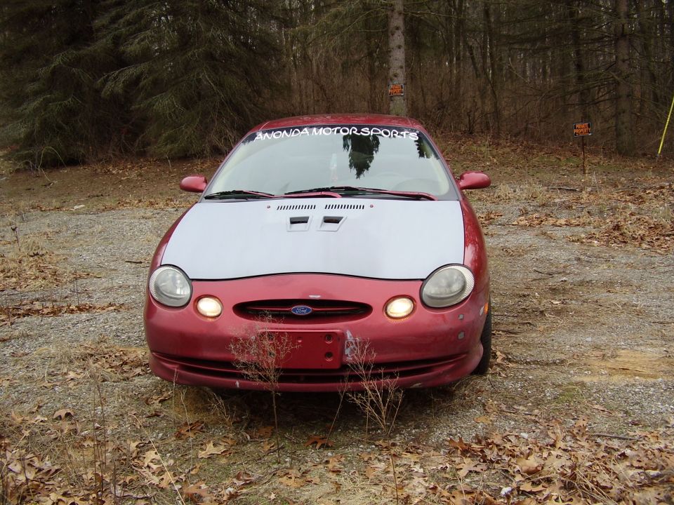 1997 Ford Taurus front view, red body with silver hood, parked outdoors