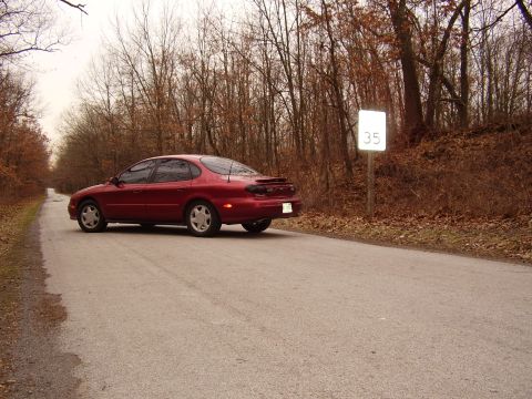 1997 Ford Taurus - A red 1997 Ford Taurus sedan is seen from the side on a paved road, with a speed limit sign indicating 35 mph visible in the background.