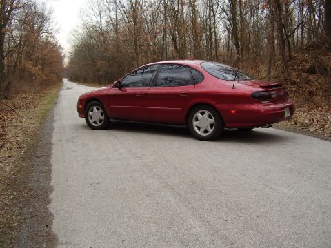 1997 Ford Taurus - Side view of a red 1997 Ford Taurus sedan on a rural dirt road.