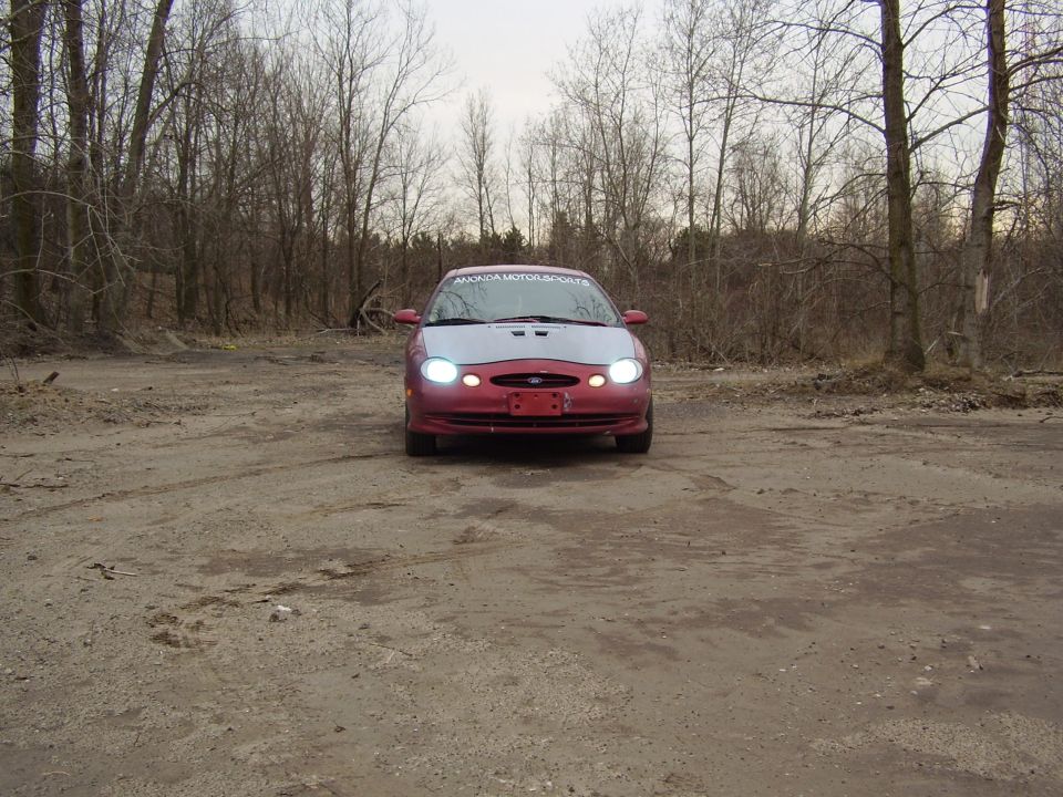 1997 Ford Taurus with a silver hood and red body, parked on a dirt lot