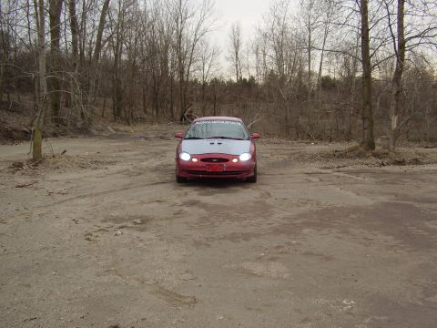 1997 Ford Taurus - A red and silver sedan is parked in an outdoor lot with trees in the background. The windshield has text on it.