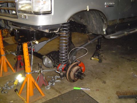 1989 Ford Bronco - The front end of a vehicle is elevated on jack stands for maintenance, revealing the suspension and axle components.