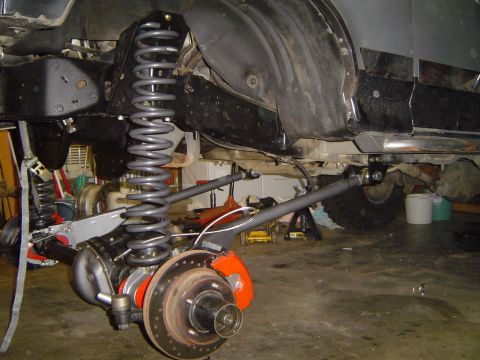 1989 Ford Bronco - Close-up view of a vehicle's rear axle and suspension system, showing a large coil spring and disc brake assembly.