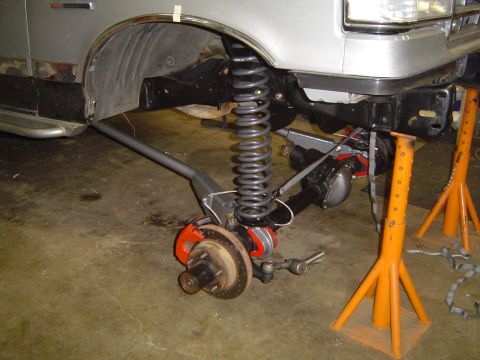 1989 Ford Bronco - The suspension and axle of a silver vehicle are being worked on, supported by orange jack stands.