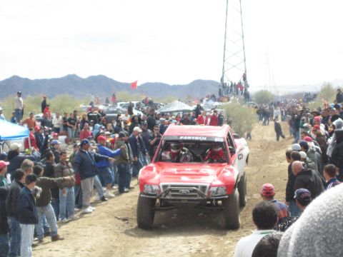 1990 Ford Bronco - red off-road race truck numbered 805 with a Ford grille emblem and Fabtech windshield banner sits among a crowd.