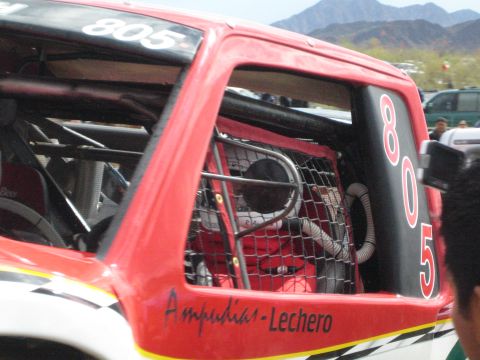1990 Ford Bronco - Close-up of a red off-road race truck's cab showing number 805, a window net, and 'Ampudia-Lechero' lettering.
