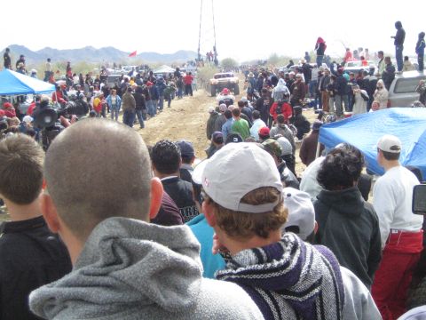 1990 Ford Bronco - crowd of spectators watches a distant off-road race truck travel a dirt track across the desert plain.
