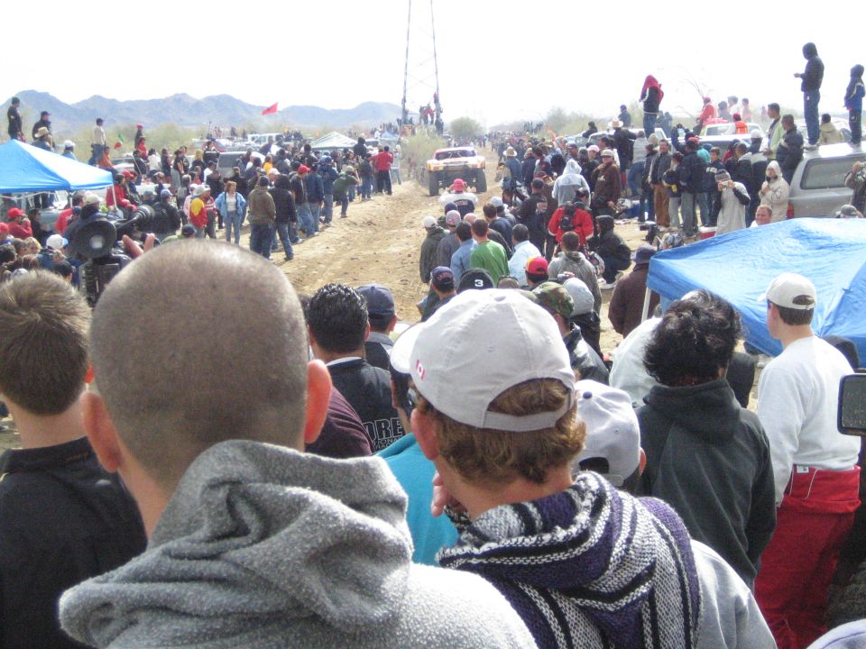 Crowd of spectators watching distant off-road truck on desert track